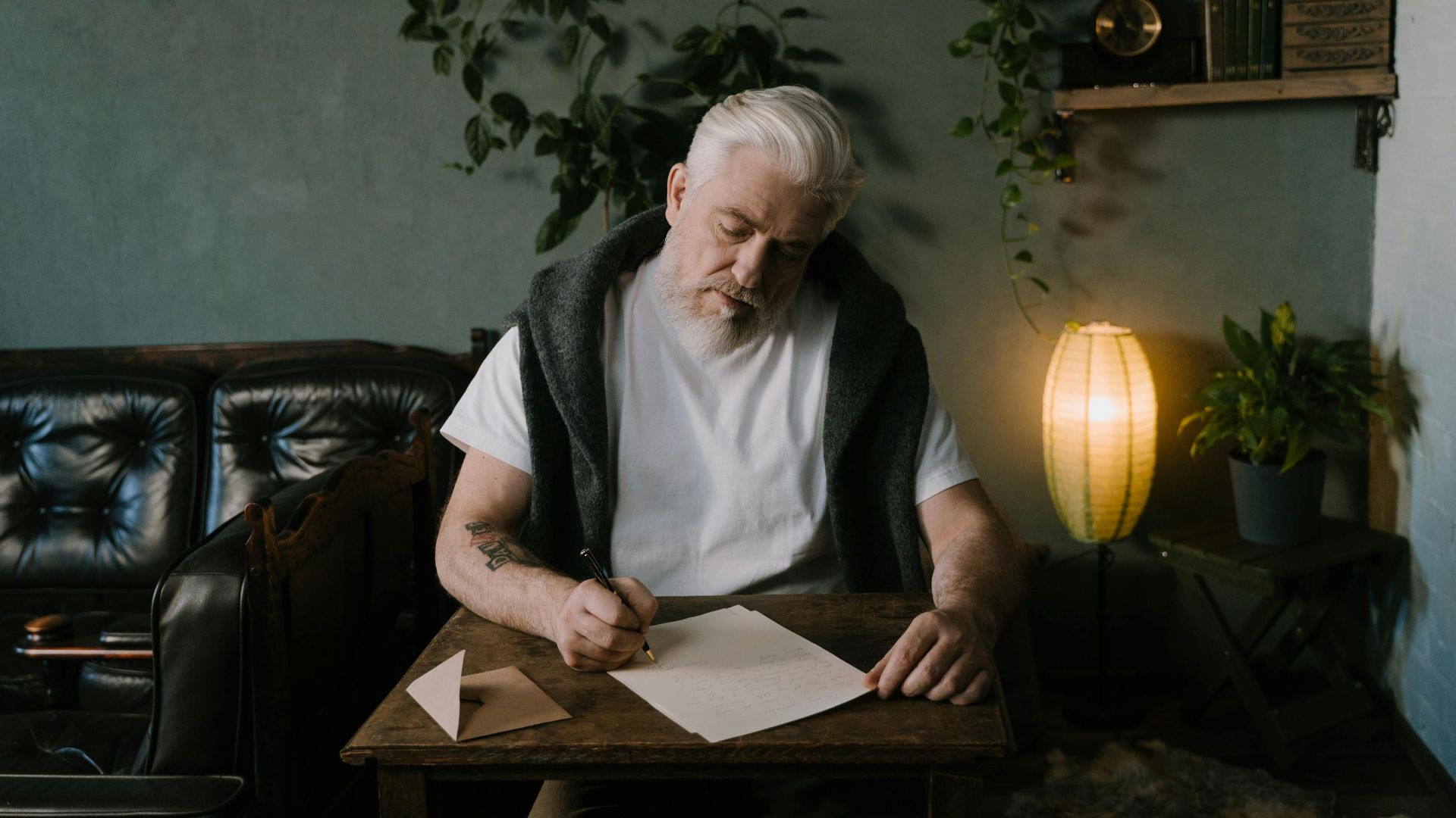 Senior man pens a letter at a wooden table in a cozy home interior.