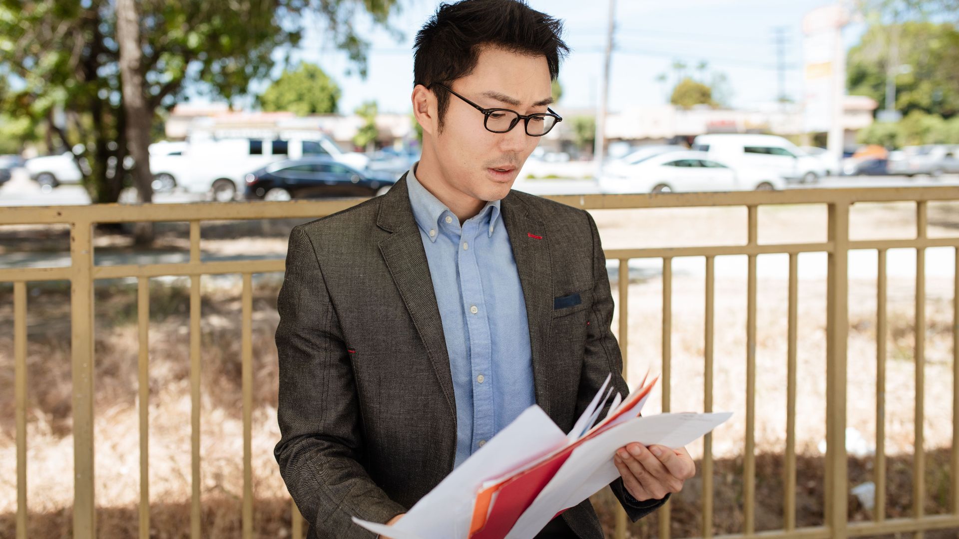 Asian businessman in a suit checking documents outdoors on a sunny day.
