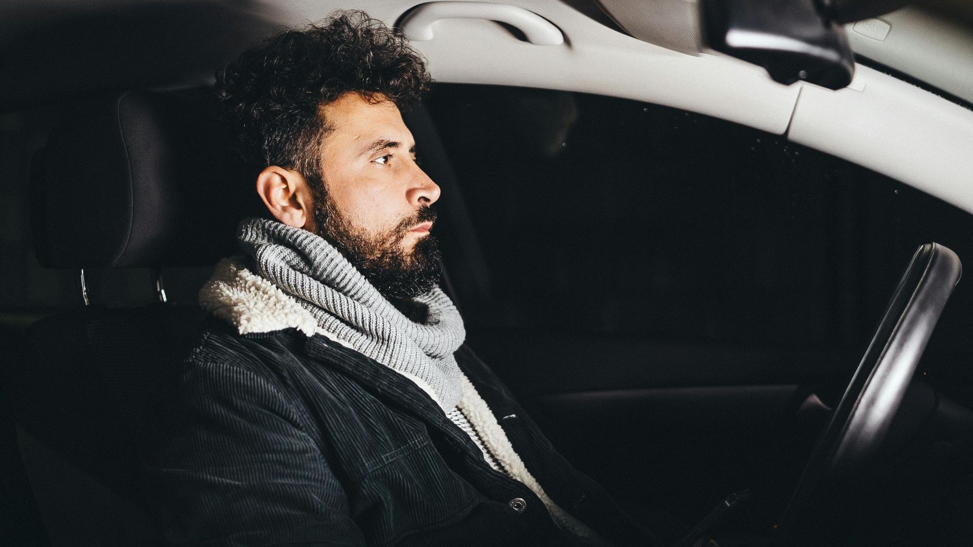 Adult man driving a car at night, illuminated and using a smartphone.