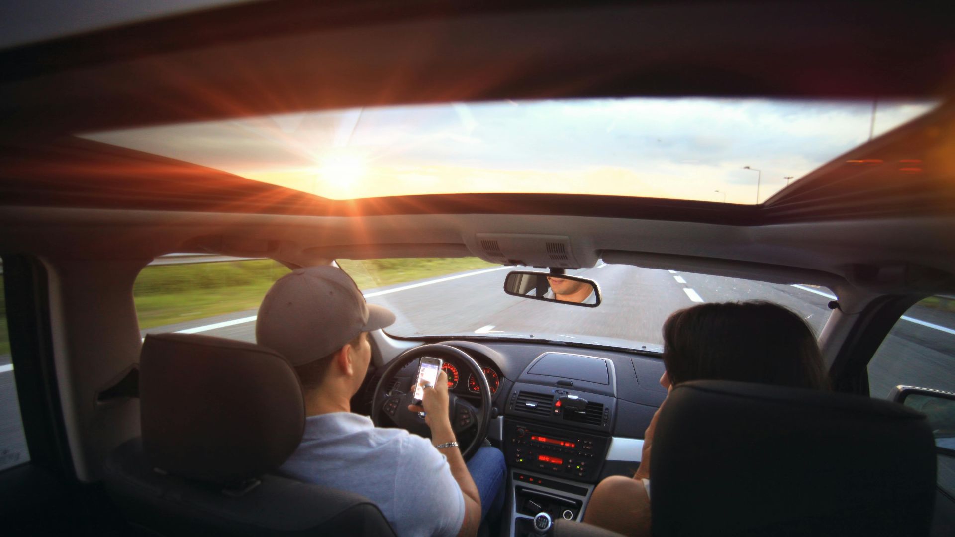 Driver using phone while driving at sunset with passenger in vehicle.