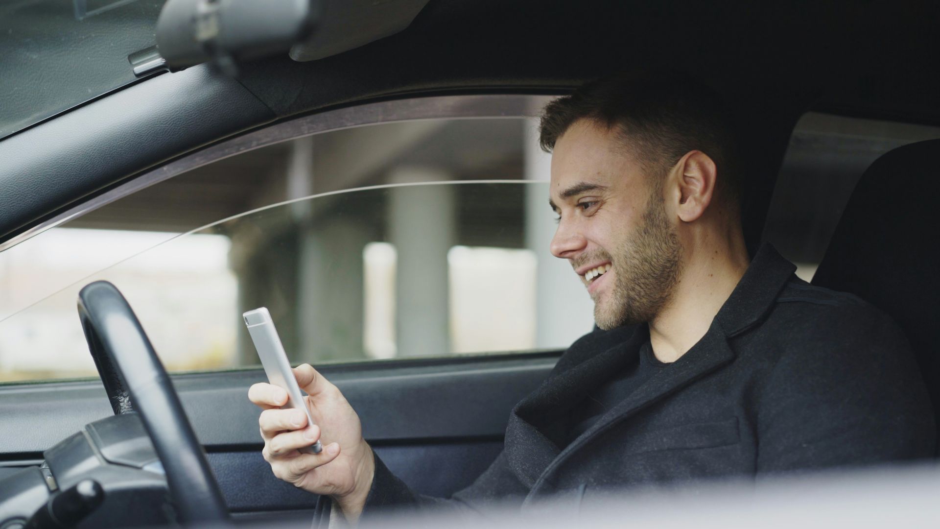 Man smiling while looking at his phone in car