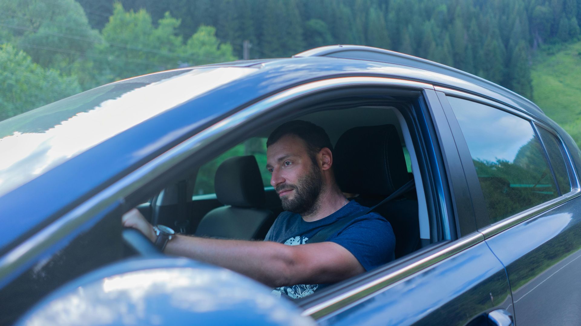 Bearded man enjoying a drive through lush green countryside on a sunny day.