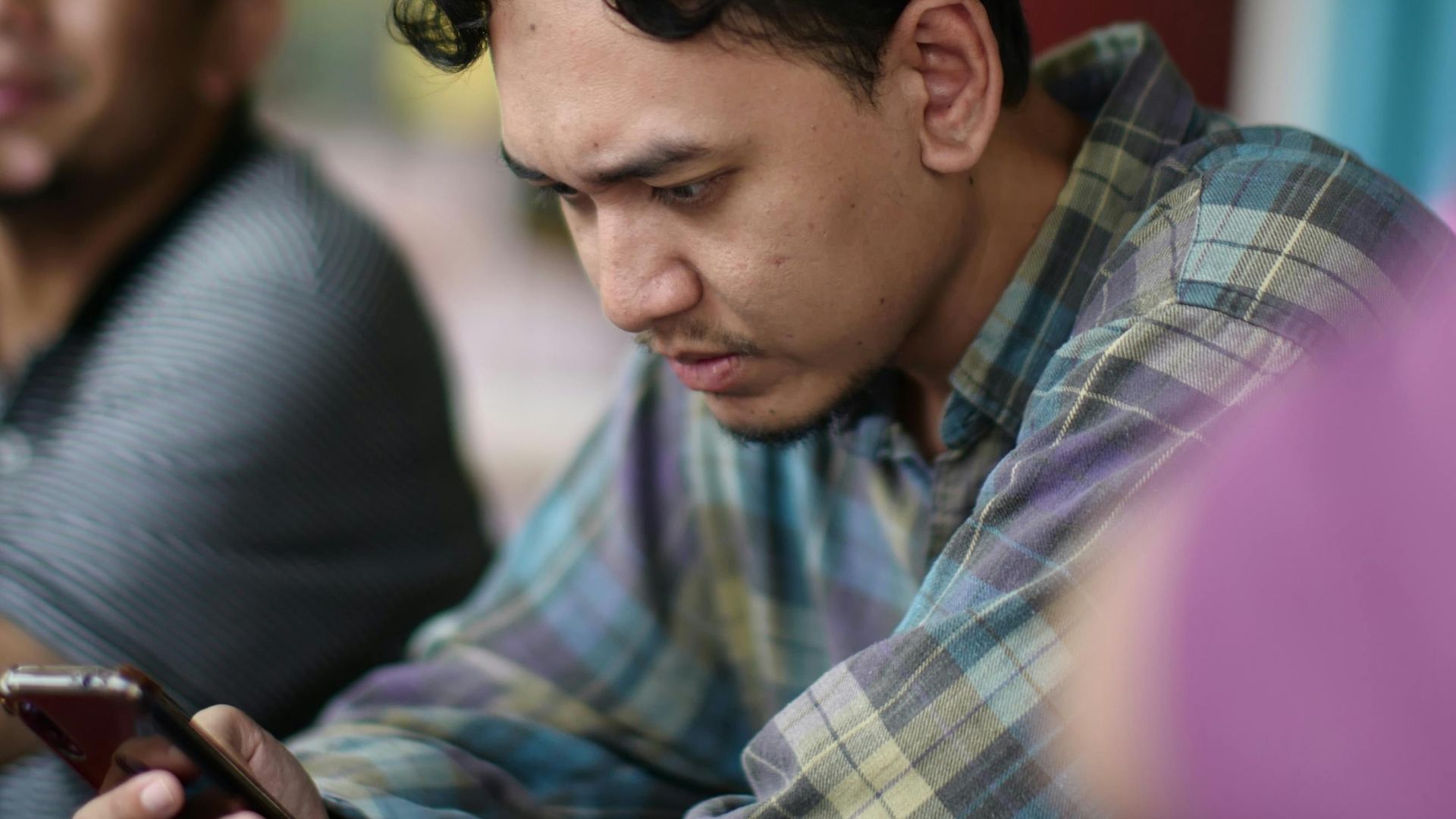 Young man focused on smartphone in a lively Kuala Dungun cafe setting.