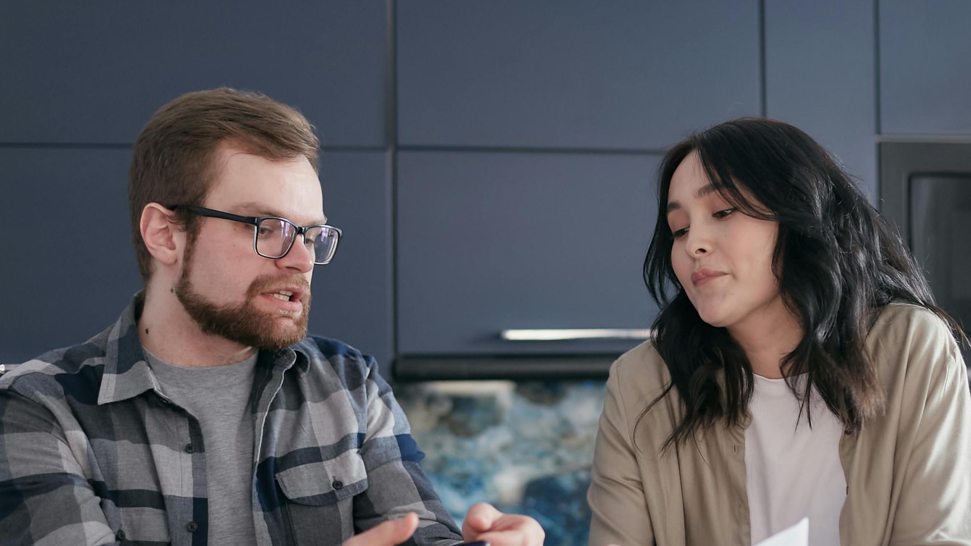 A couple sits at a kitchen table reviewing documents and discussing finances.