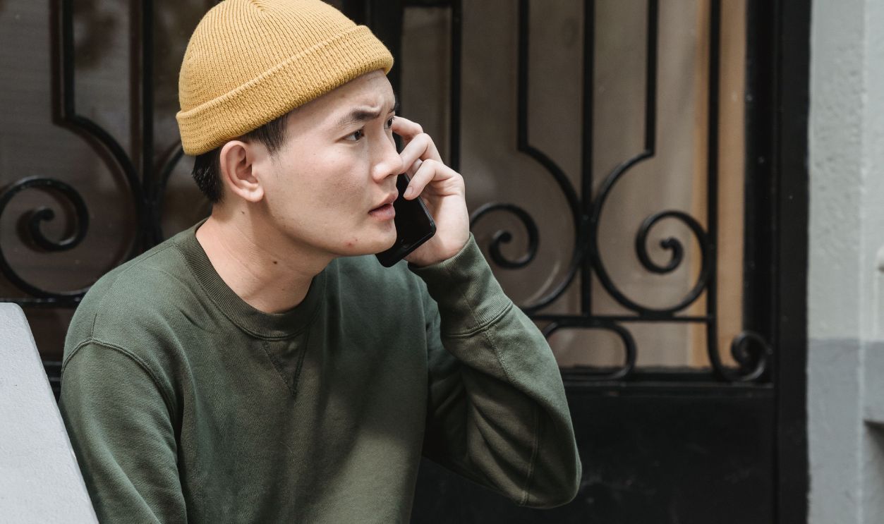 Young man in casual attire sitting on steps, talking on the phone in an urban setting