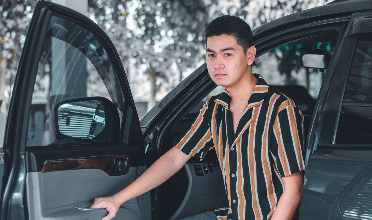 Portrait of a young man with a striped shirt standing beside an open car door