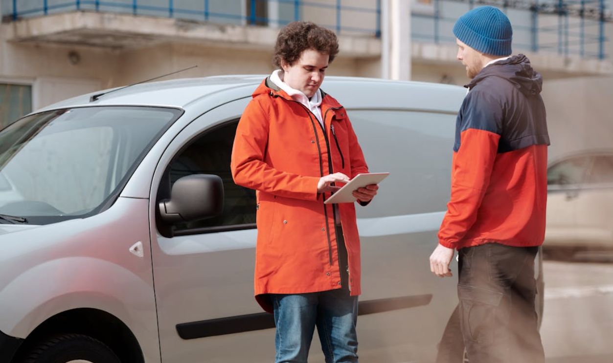 Two delivery men in bright jackets using a digital tablet beside a van outdoors