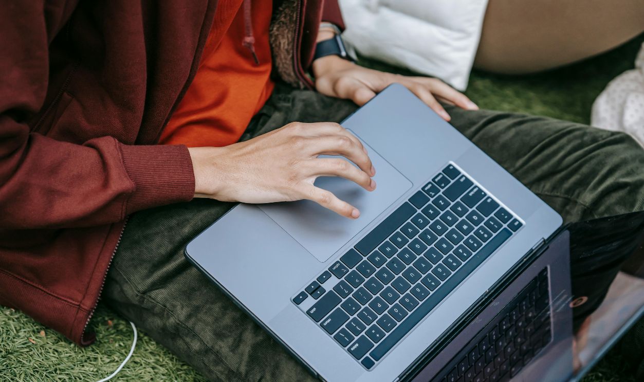 A young adult working on a laptop while sitting on grass, focused on study or research, outdoors