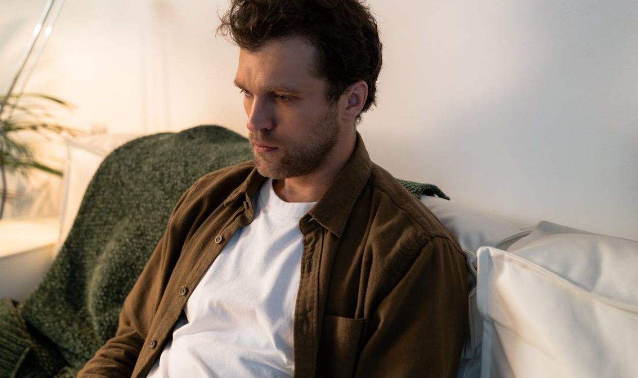 A thoughtful man sitting indoors, reflecting quietly on a sofa in a cozy ambiance