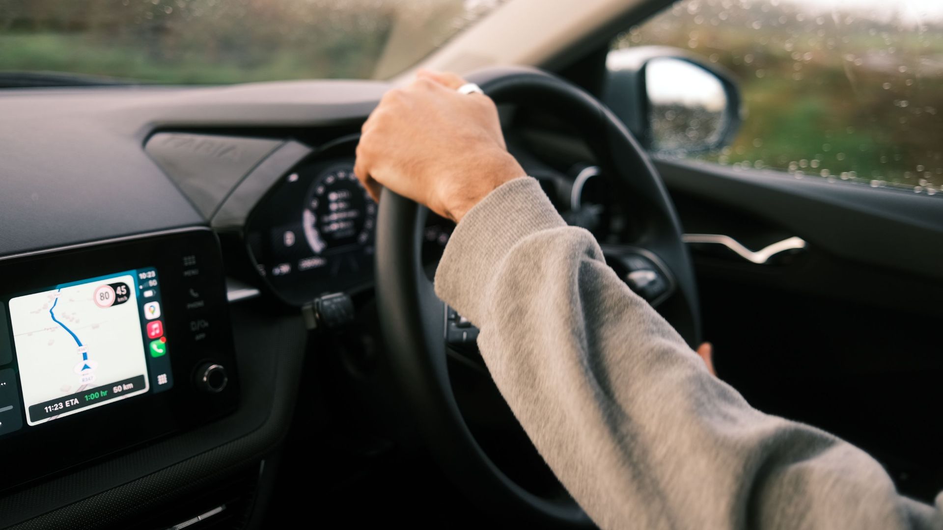 A person drives through rainy conditions, guided by GPS technology on their dashboard.