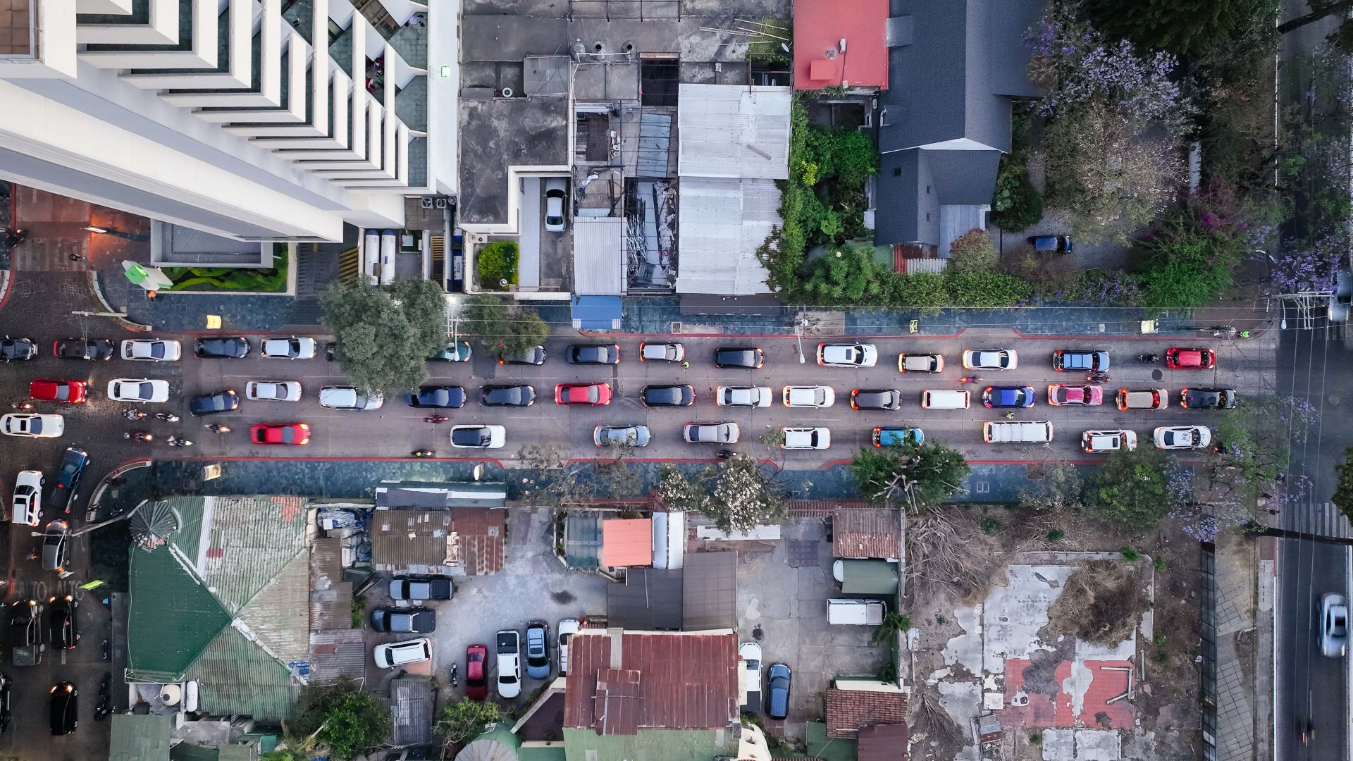 Drone aerial shot depicting urban traffic congestion on a city street surrounded by buildings.