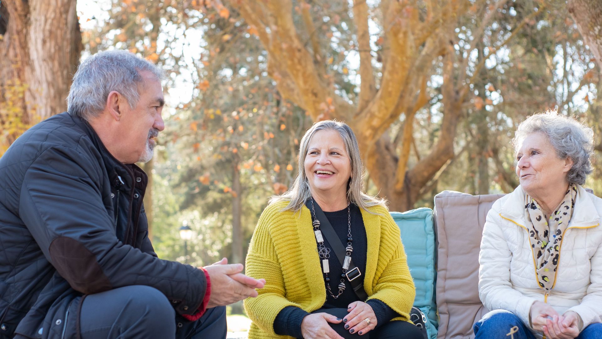 Three senior adults enjoying tea outdoors on a wooden table in Portugal's forest park.