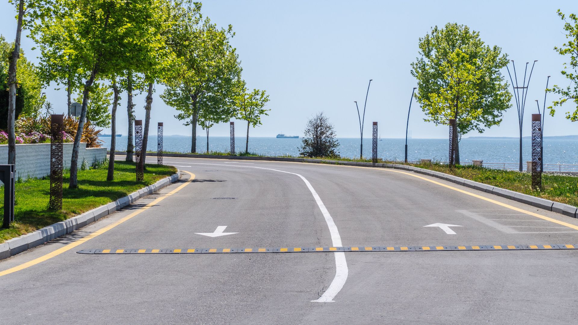 A curved road by the sea in Baku, Azerbaijan, lined with trees and clear blue skies, offering a peaceful scene.