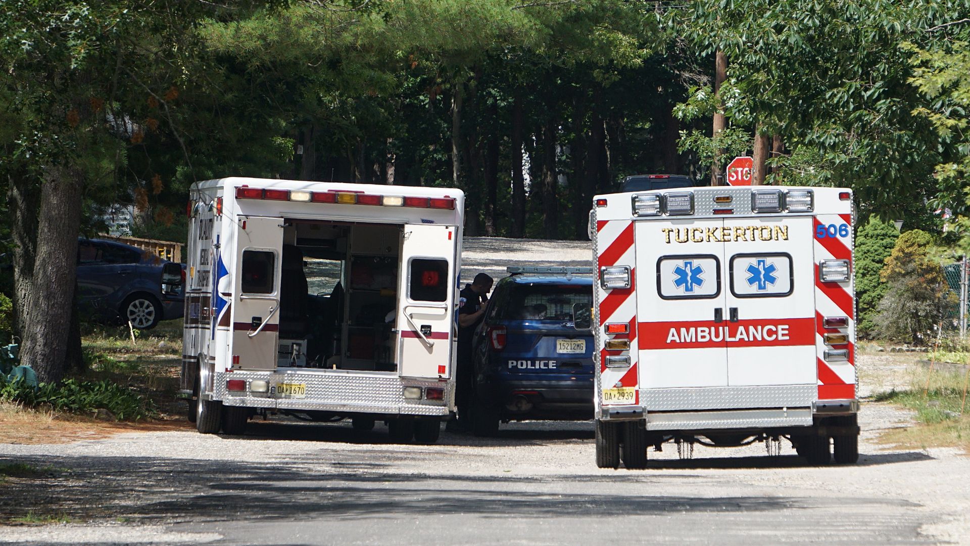 Ambulances and a police car on a tree-lined road responding to an emergency.