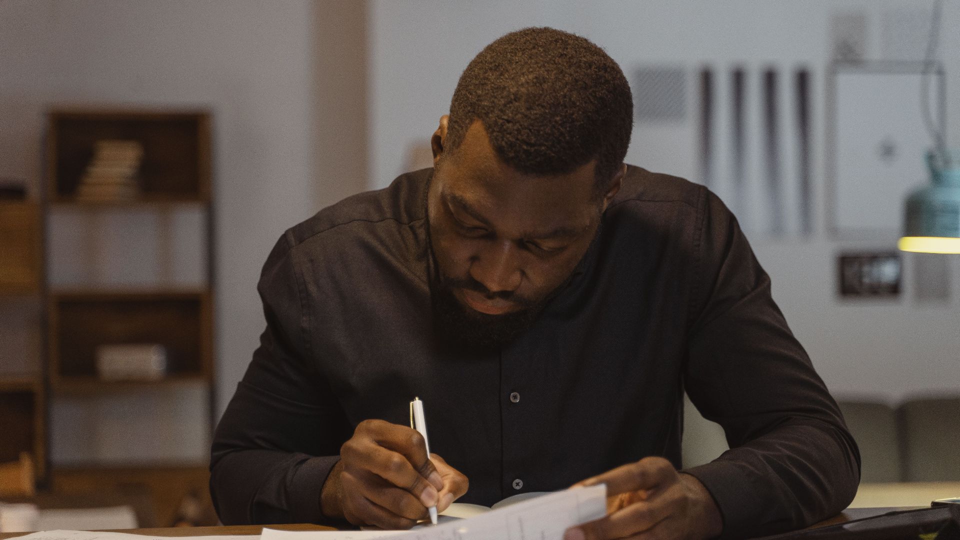 A man diligently writing notes in a modern office environment. Perfect for business and productivity themes.