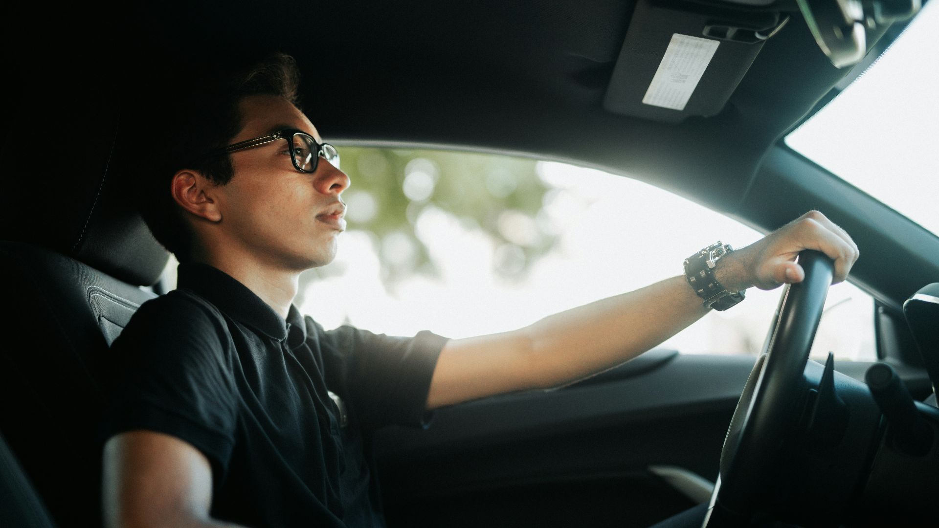 a man driving a car with his hand on the steering wheel