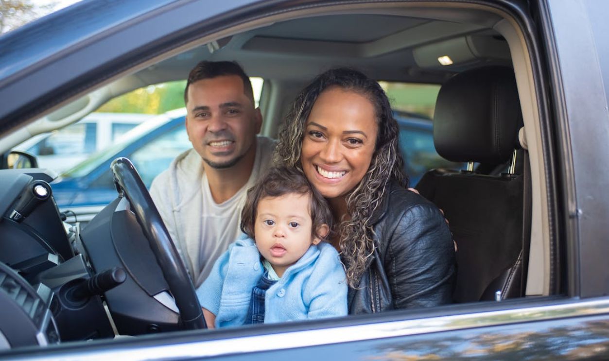 A joyful family with a baby in a car, expressing happiness and togetherness.