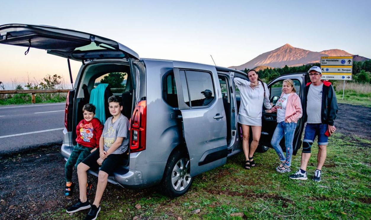 A family enjoys a scenic road trip by Mount Teide, Spain, with a van parked by the roadside.