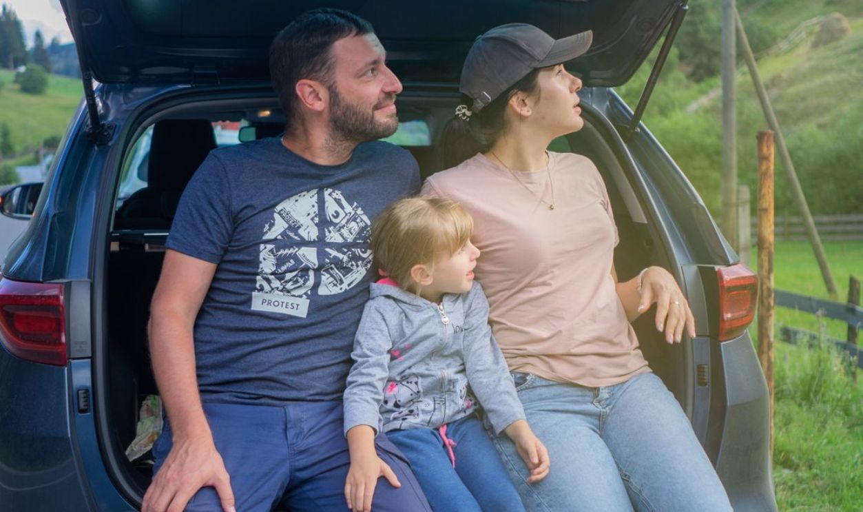 A family sits in a car trunk, enjoying an outdoor adventure in a scenic countryside.