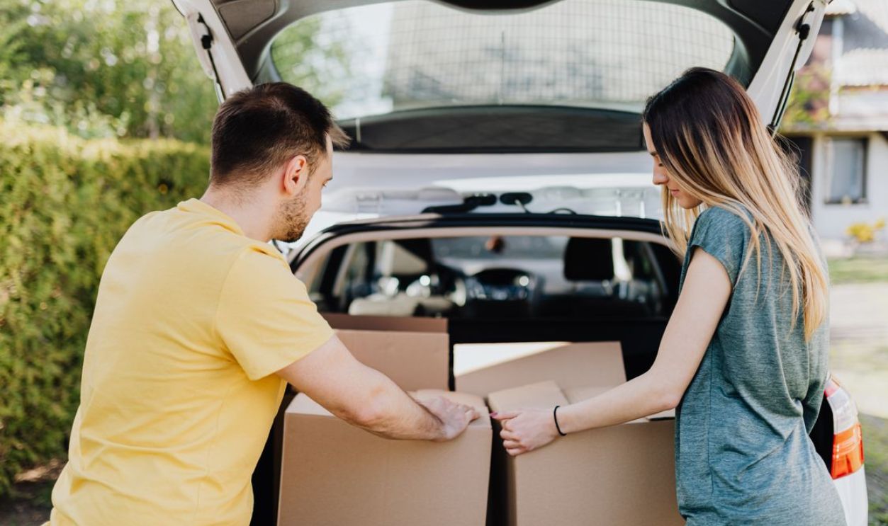 A couple loading cardboard boxes into a car trunk for moving day.