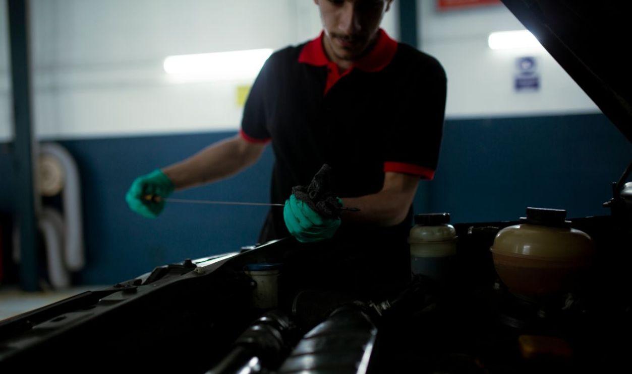 Mechanic examining a car engine's oil level using a dipstick in a garage setting.