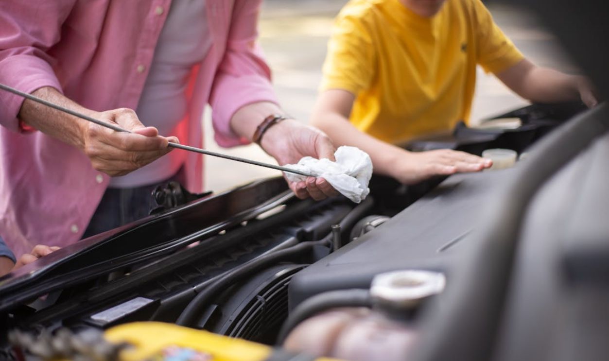 Father and son working on car maintenance, checking engine oil outdoors.