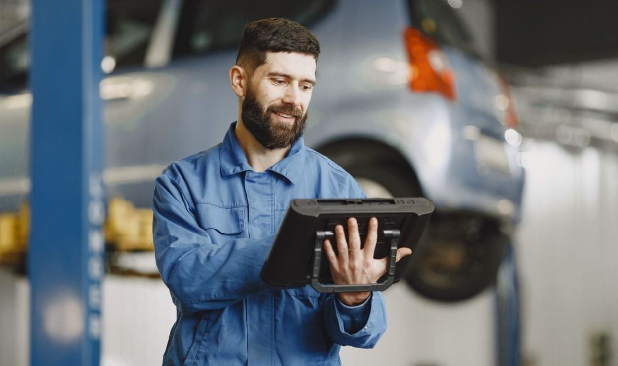 Smiling auto mechanic uses digital tablet in car repair shop environment.