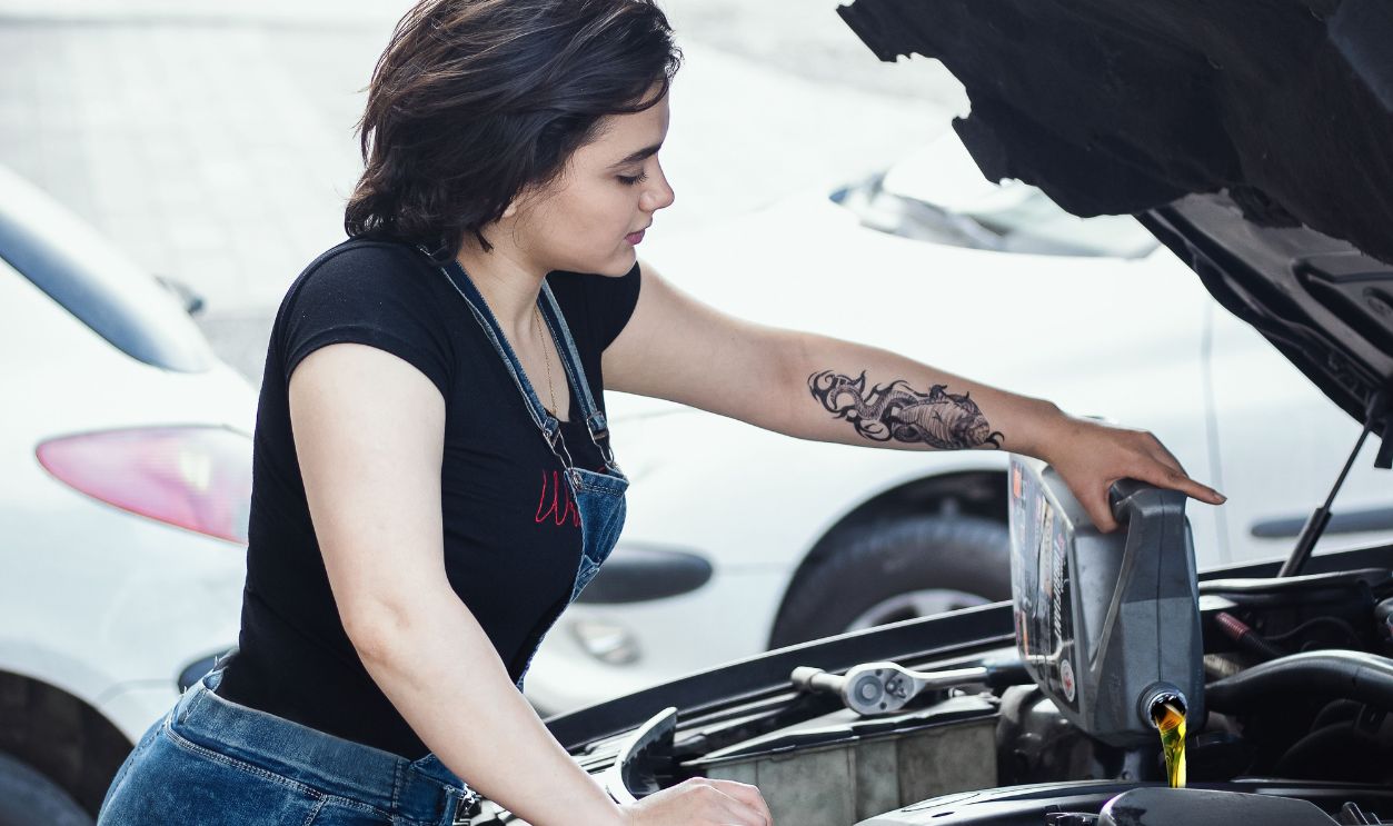 Woman adding oil to a car engine outdoors in Rasht, Iran, showcasing DIY vehicle care.