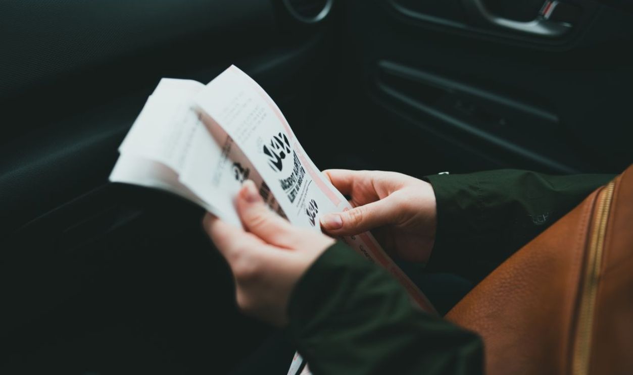 Close-up of hands holding a brochure inside a car, creating an intimate and focused scene.