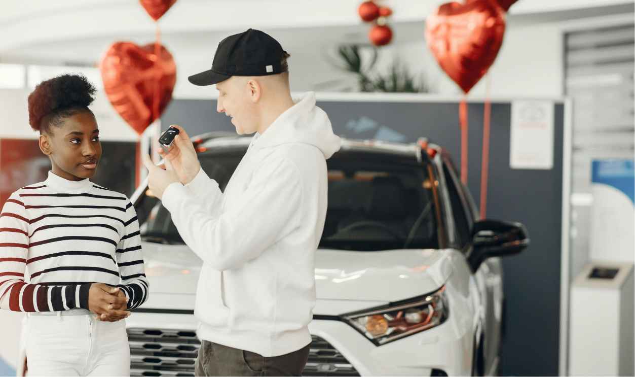 A couple exchanging car keys inside a showroom decorated with heart-shaped balloons