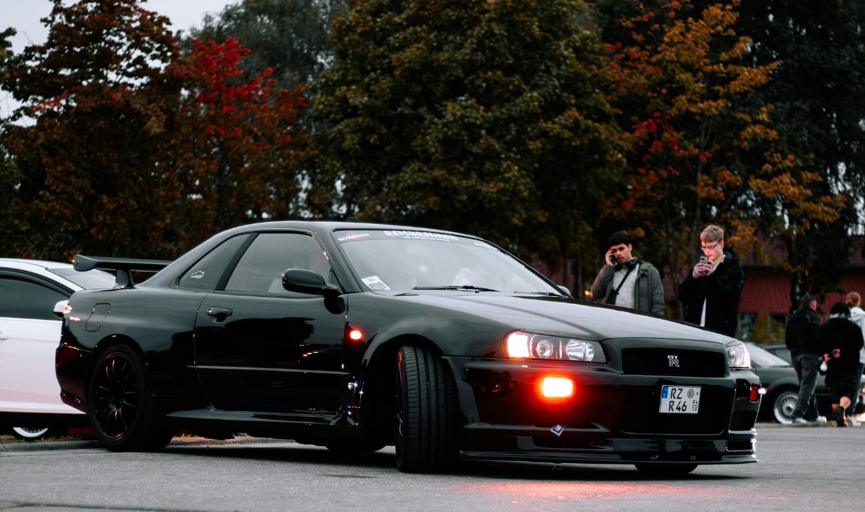 A sleek black sports car showcased at a car meet surrounded by colorful autumn foliage