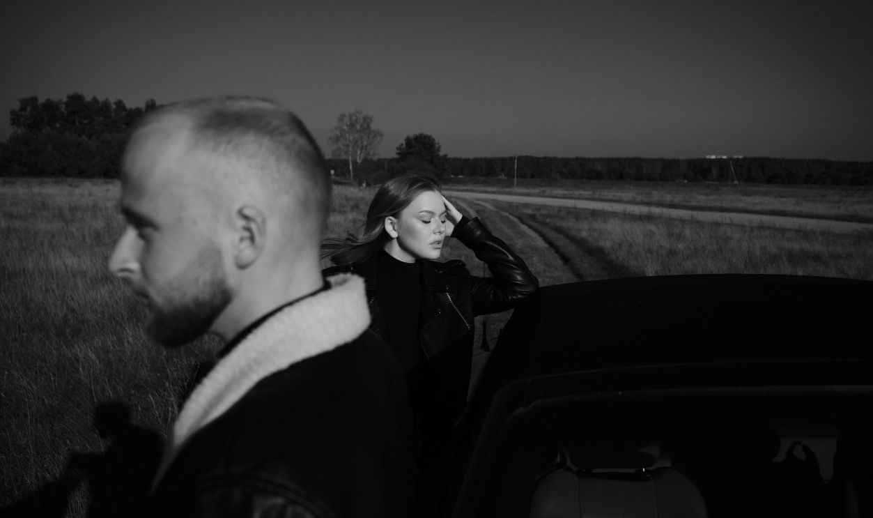 A man and woman in a moody black and white outdoor setting, capturing a blend of contemplation and style