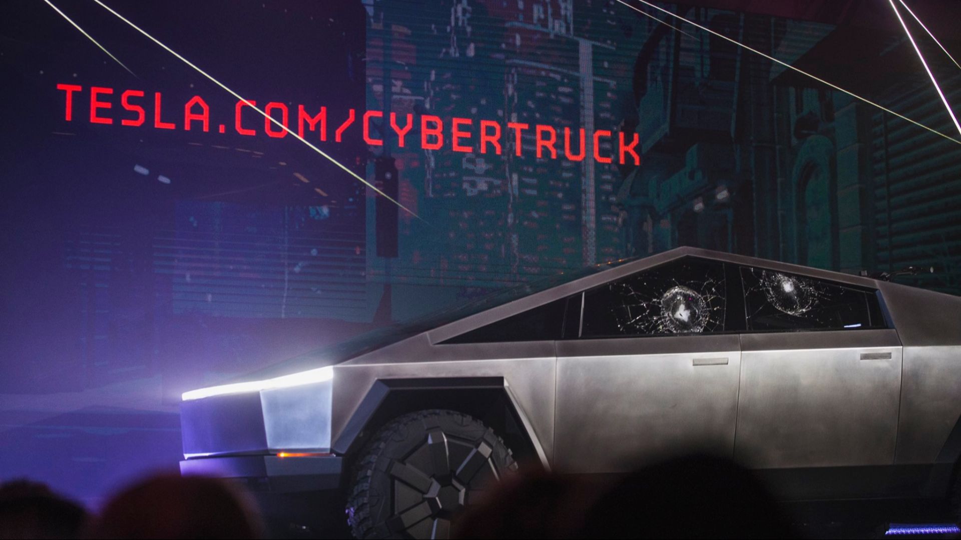 Tesla Cybertruck with shattered windows and tesla.com/cybertruck URL during presentation.  The broken windows were replaced afterwards, prior to the test rides.