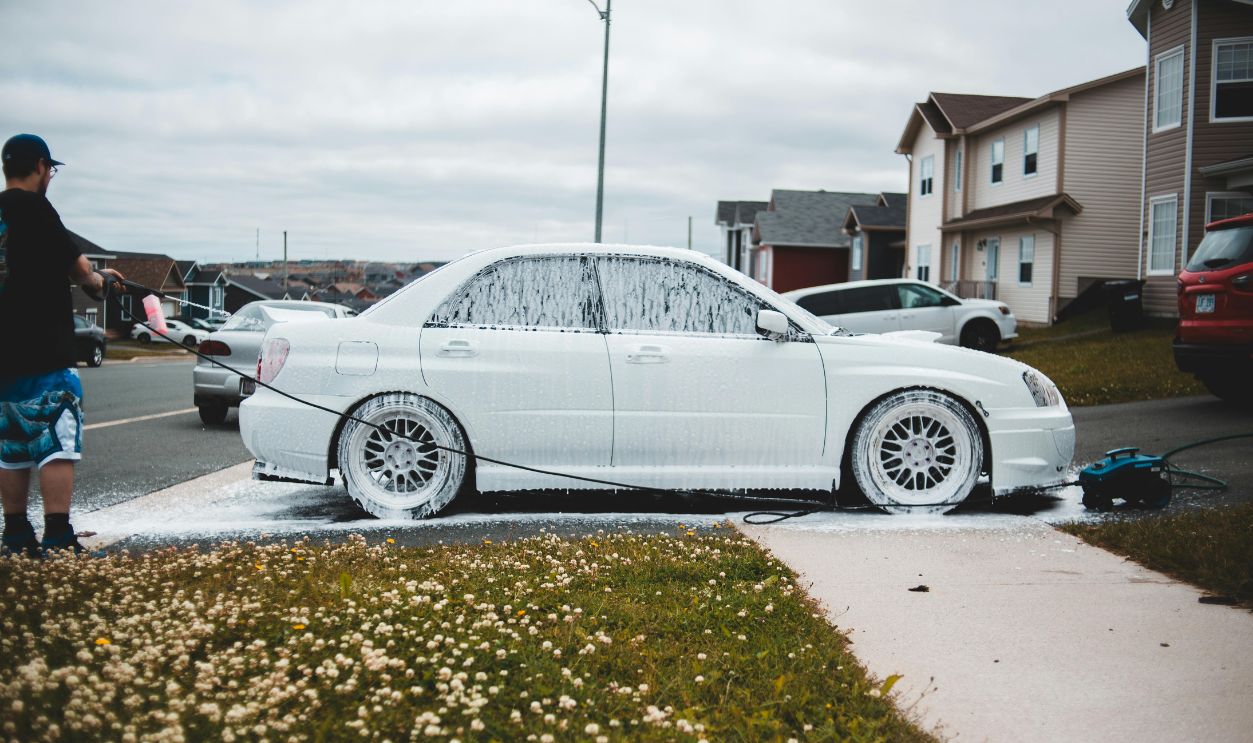 A man pressure-washes a car with foam