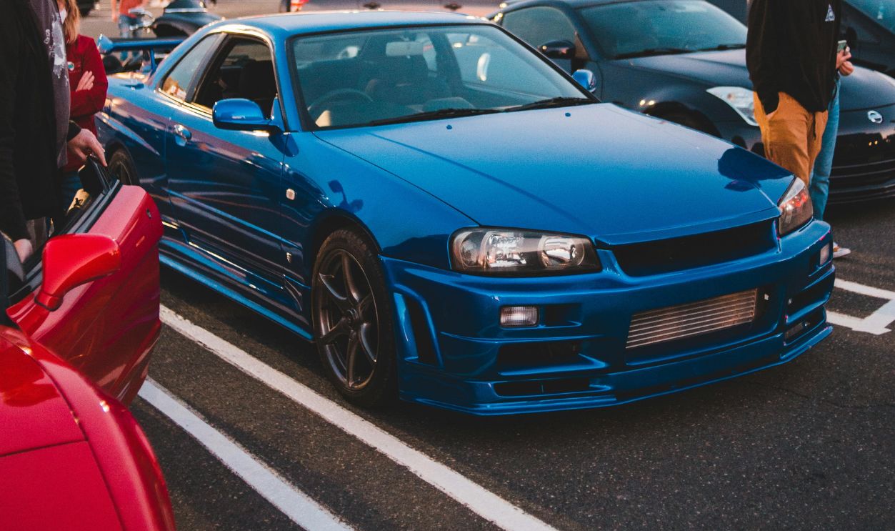A vibrant blue sports car parked in a busy lot at dusk, surrounded by people.