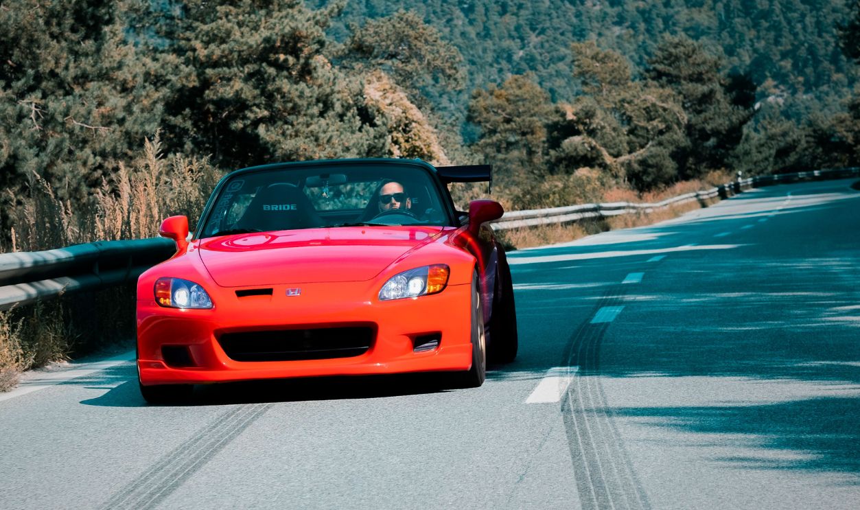 A vibrant red convertible speeds through a scenic mountain road in Sion, Switzerland, showcasing automotive elegance