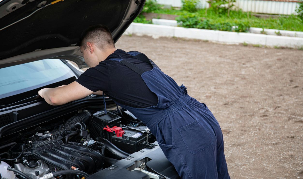 Mechanic in blue coveralls working on a car engine outdoors