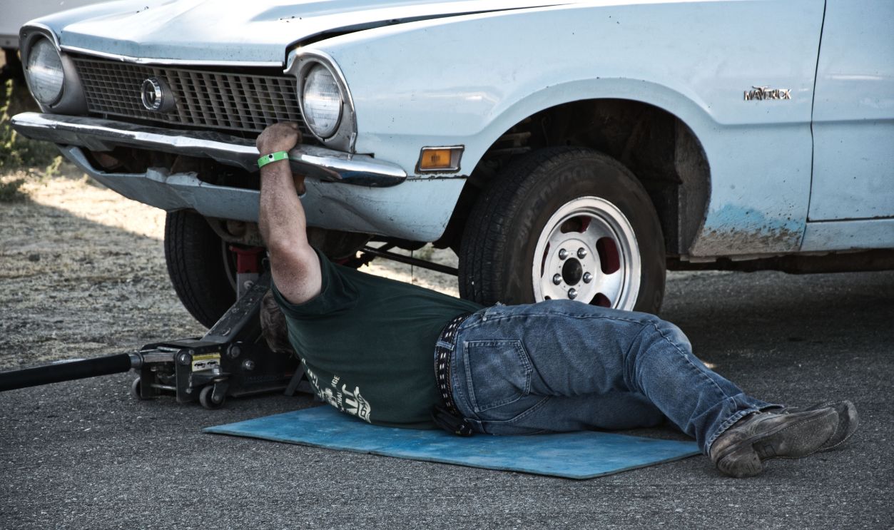 A mechanic working under a classic car on the pavement 