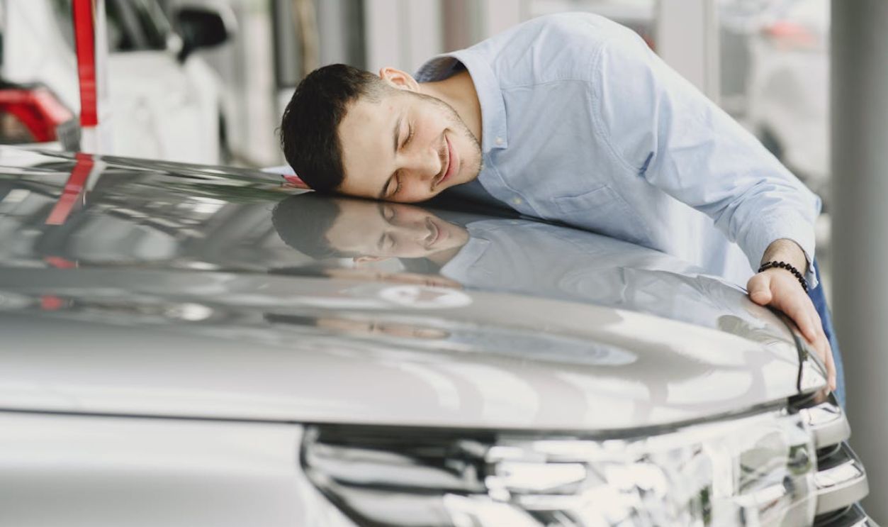 A man joyfully embracing a new car indoors, reflecting happiness and satisfaction.