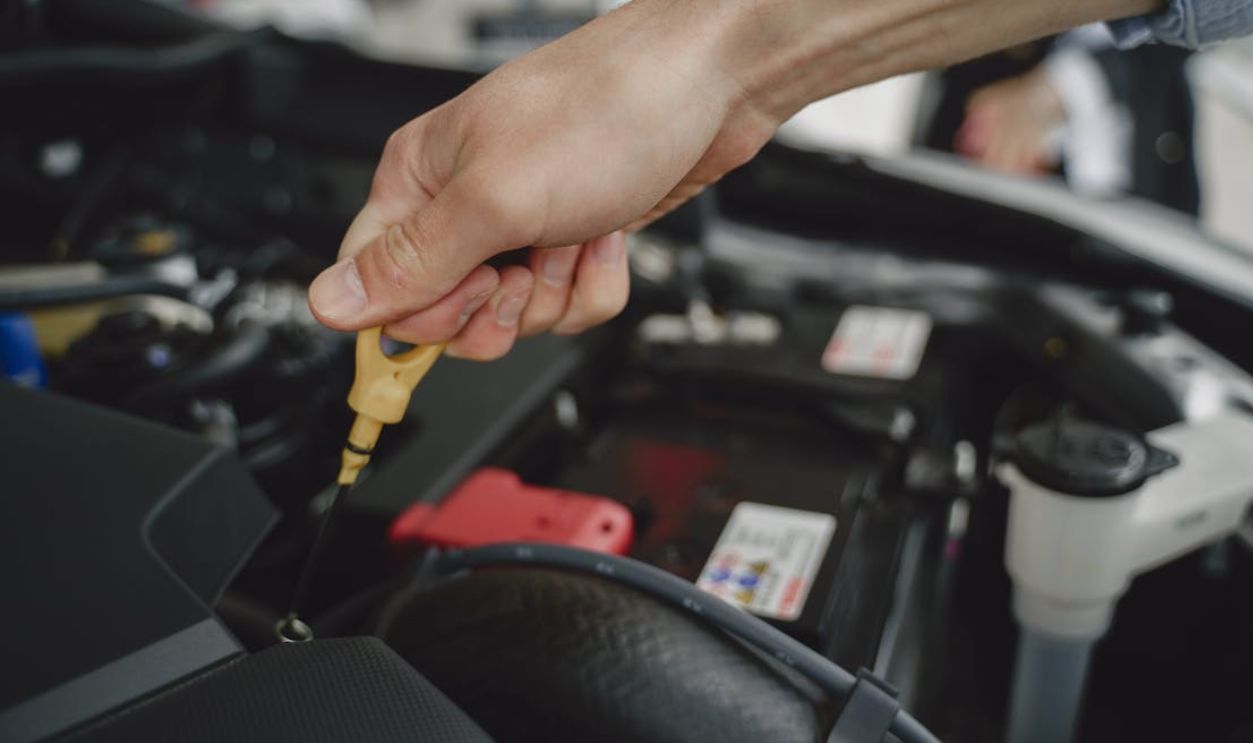 Hand checking oil dipstick in a car engine bay for maintenance and diagnostics