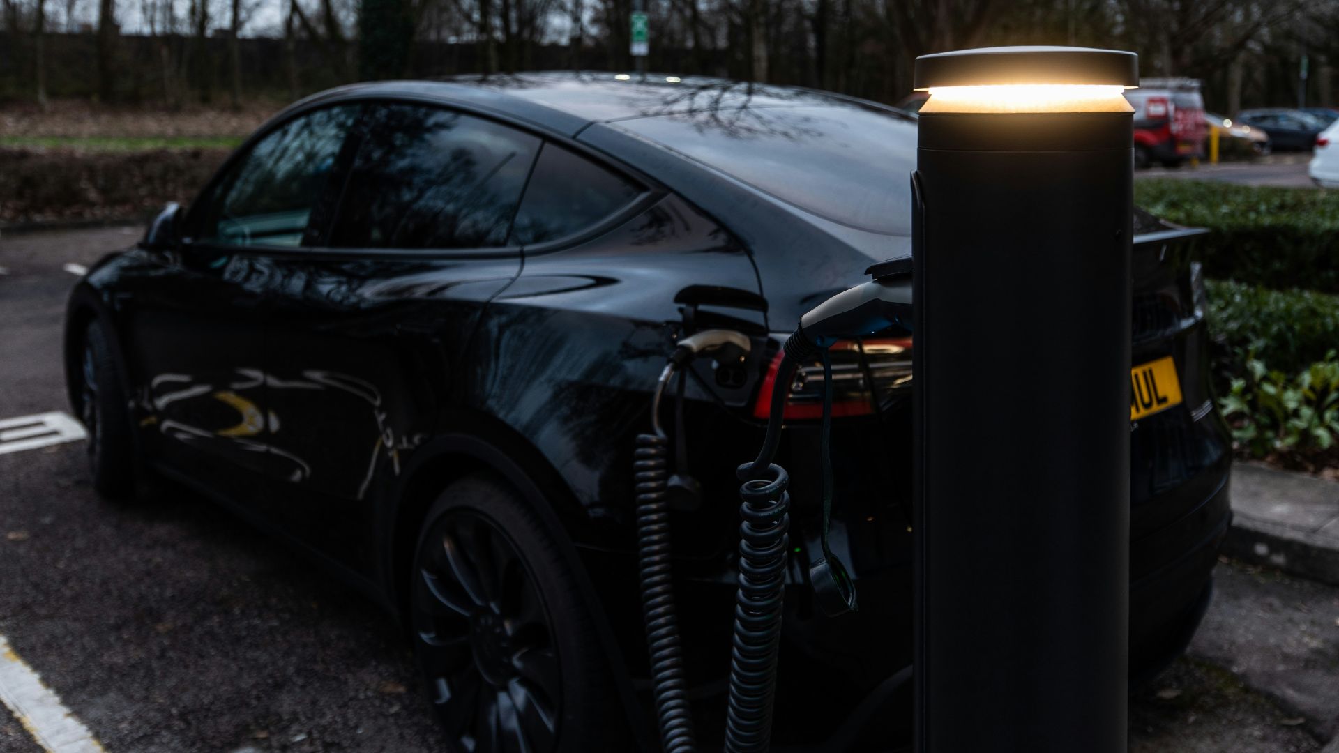 Black electric car charging at an outdoor station.