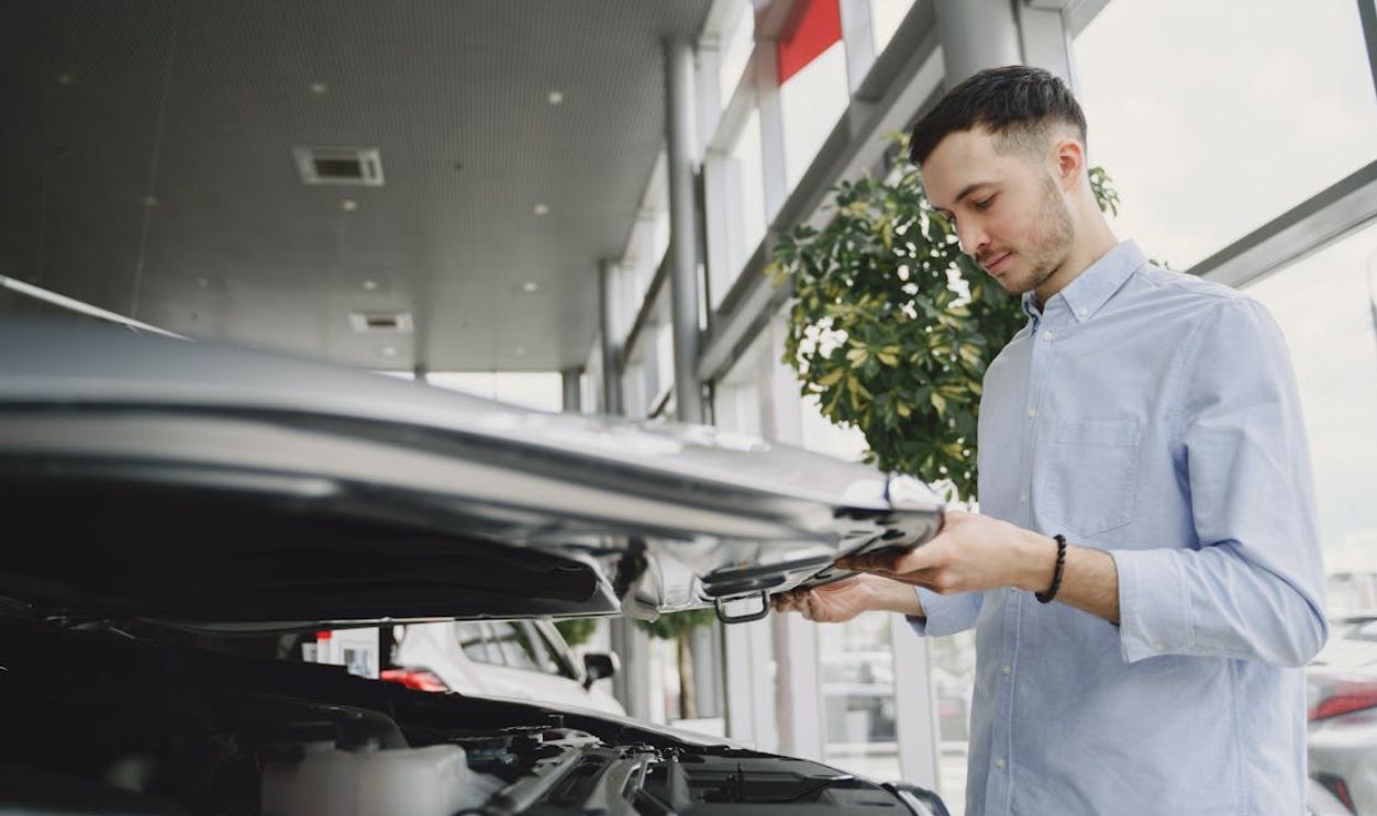 Young man checking car engine in modern dealership showroom