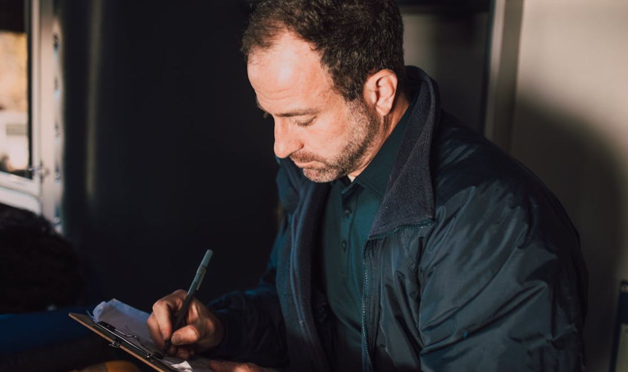 Adult male writing notes on a clipboard inside. Concentrated and thoughtful atmosphere