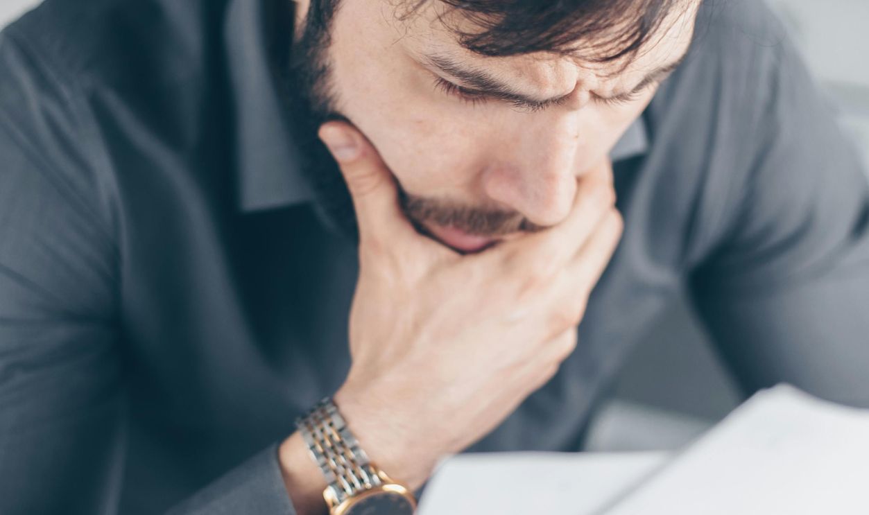 Man in gray shirt with glasses looking concerned over financial papers