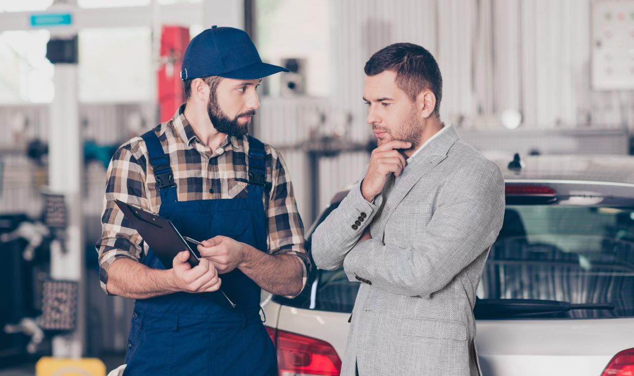 Experienced brunet bearded expert specialist in blue overall is discussing and demonstrates the demages of businessman`s car, he is ponder pensive, focused and concentrated, decisions, options
