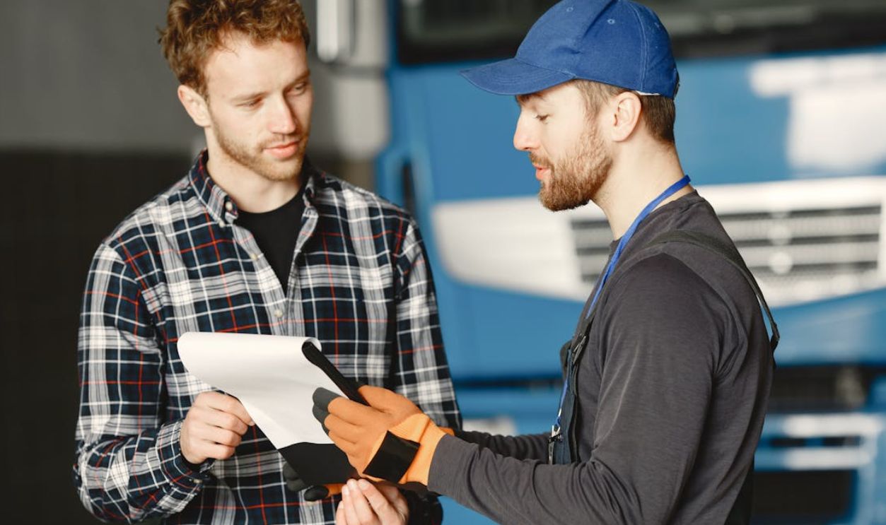 Mechanic in uniform talks with a customer about vehicle maintenance inside a garage