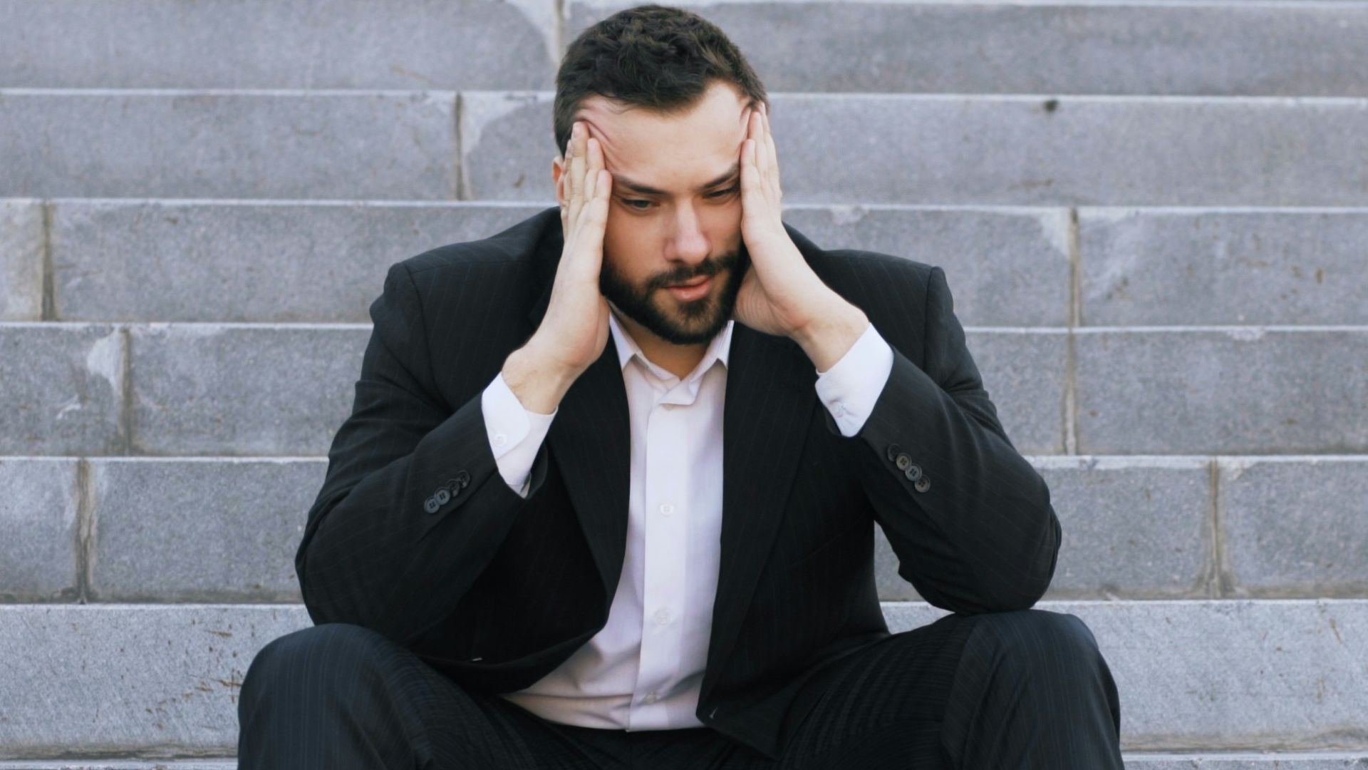 Man in suit sitting on stairs with head in hands