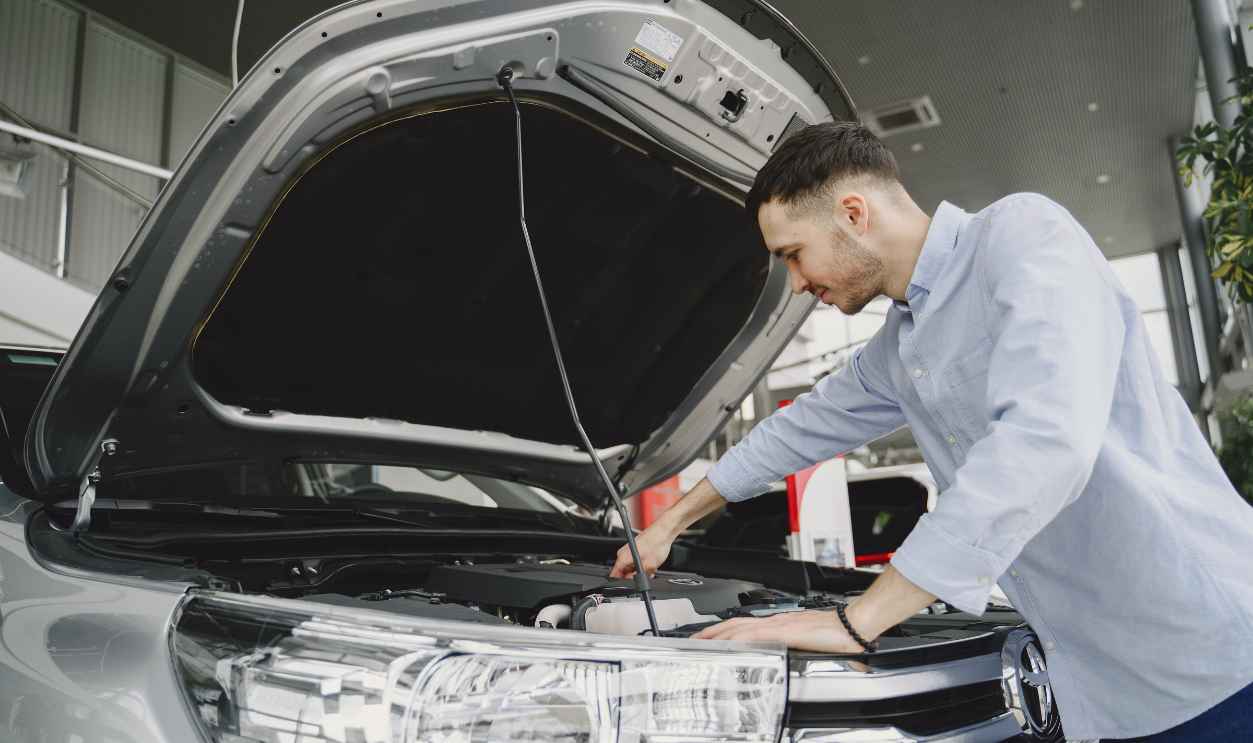 A man in a blue shirt examines a car's engine in a modern vehicle