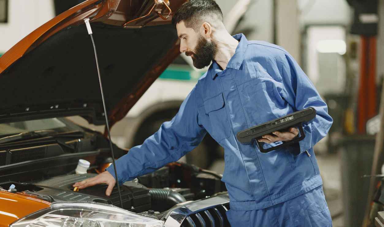 Professional mechanic examining a car engine under an open hood in a garage setting.