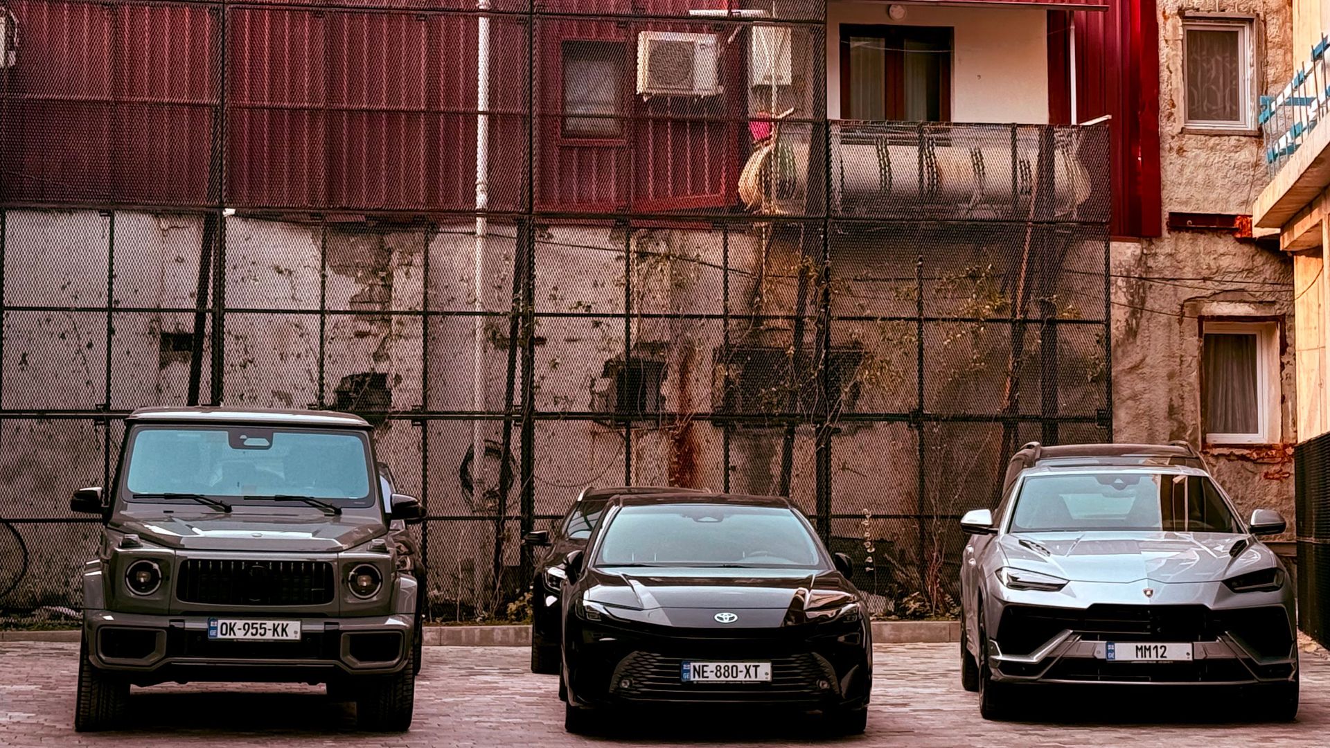 Three cars parked in an urban area with a red building and decorative architecture in the background.